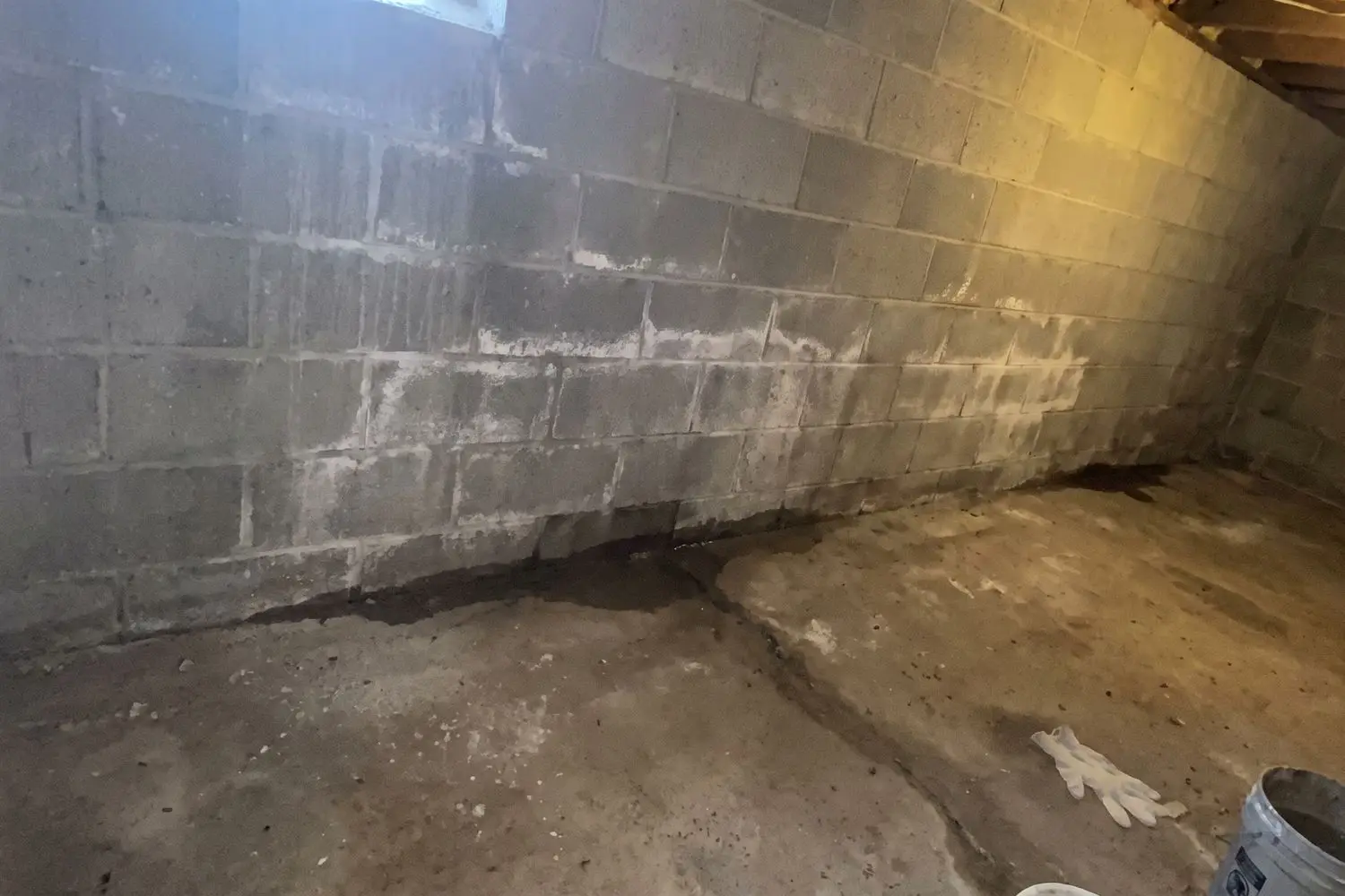 White efflorescence and dark water staining on a concrete block basement wall, with seepage along the cove joint where the wall meets the floor slab