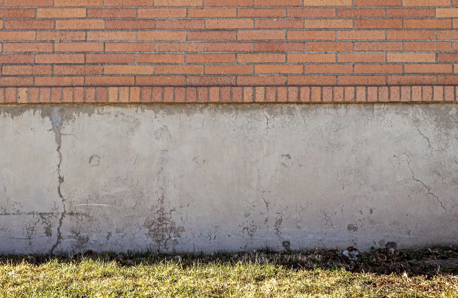 Exterior poured concrete foundation wall at the base of a brick home, meeting the grass at grade