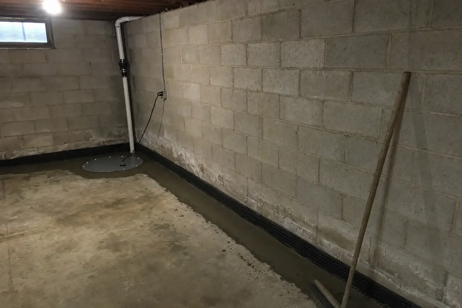 Finished interior drain tile installation in a block basement: new concrete strip along the wall, dimpled membrane at the cove joint, and a sealed sump basin